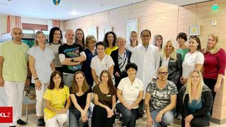 Eine Gruppe von medizinischem Fachpersonal und Mitarbeitern, darunter einige in weißen Kitteln, posiert für ein Foto in einem Raum mit beigen Wänden.