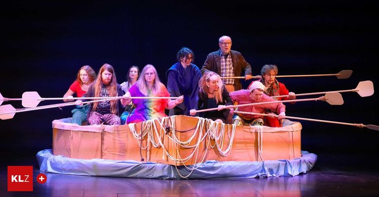 Eine Gruppe von Menschen ist auf der Bühne und rudert ein Pappboot, trägt verschiedene Kostüme und hält Paddel.