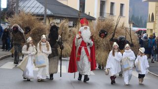 Eine Gruppe von Menschen in Kostümen, die an einem Umzug teilnehmen. Der Weihnachtsmann führt den Umzug an, gefolgt von einigen Teufeln in Kostümen.