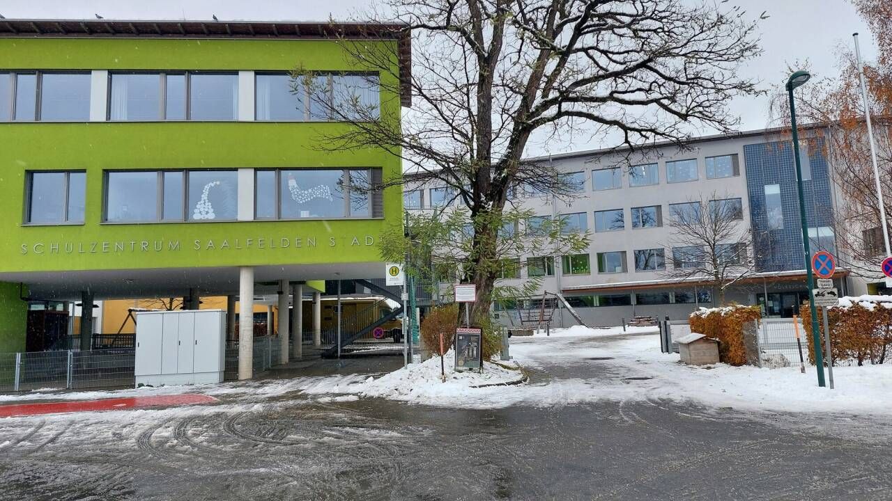 Ein grünes Gebäude mit der Aufschrift Saalfelden Sad steht vor einem größeren, schneebedeckten Gebäude. In der Aufnahme sind keine Menschen zu sehen.