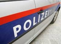Eine Nahaufnahme der Seite eines Polizeiwagens mit dem Wort 'POLIZEI' in Weiß, roten und blauen Streifen auf einer grauen Oberfläche.