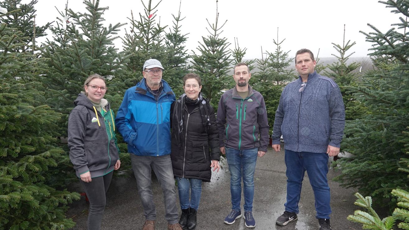 Fünf Personen, darunter zwei Frauen, stehen in einer Reihe vor einem Kiefernwald, gekleidet in Winterkleidung.