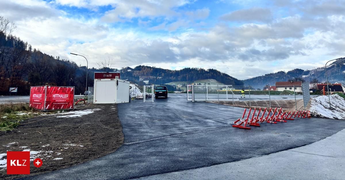 Ein offenes Gelände mit einer neuen Asphaltstraße und einem roten Banner, mit Bergen im Hintergrund.