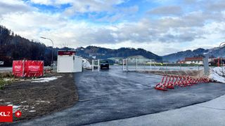 Ein offenes Gelände mit einer neuen Asphaltstraße und einem roten Banner, mit Bergen im Hintergrund.