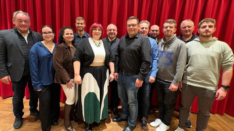 Eine Gruppe von Menschen posiert vor einem roten Vorhang für ein Foto. Sie alle lächeln und schauen in die Kamera.