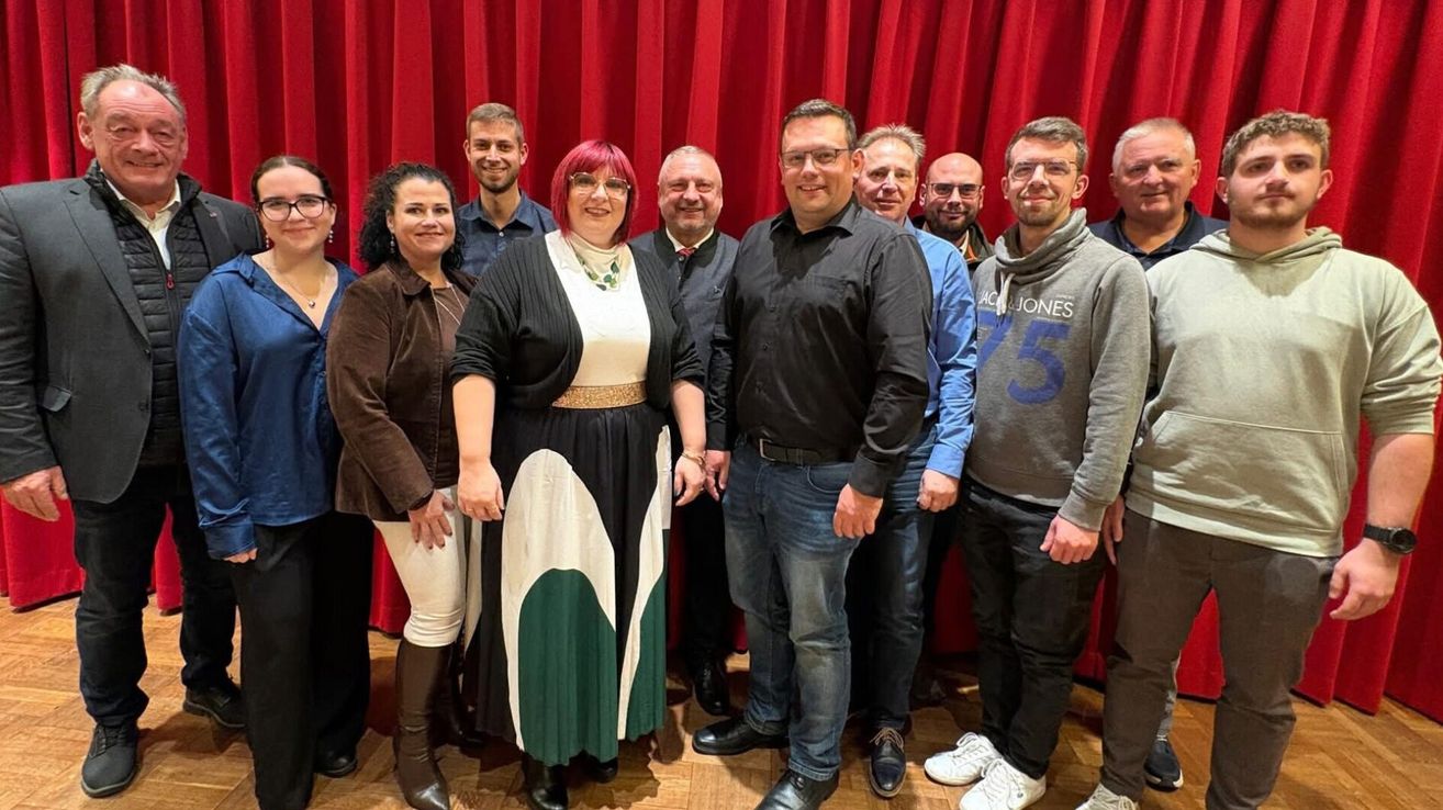 Eine Gruppe von Menschen posiert vor einem roten Vorhang für ein Foto. Sie alle lächeln und schauen in die Kamera.