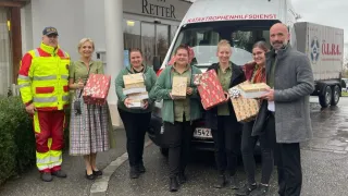 Eine Gruppe von Freiwilligen steht vor einem weißen Van mit der Aufschrift Katastrophenhilfedienst. Sie halten alle Geschenke in den Händen. Dahinter befindet sich ein Gebäude mit dem Namen Retter.
