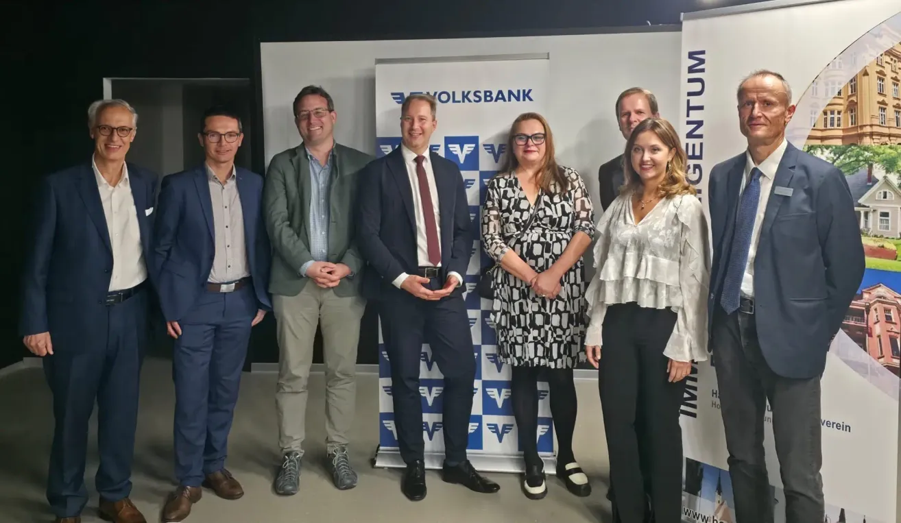 Sechs formell gekleidete Personen stehen vor einem Volksbank-Schild und lächeln für ein Foto.