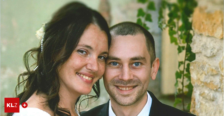 Ein frisch verheiratetes Paar, beide lächelnd, steht eng beieinander, wahrscheinlich auf ihrer Hochzeit. Die Frau hat eine Blume im Haar.