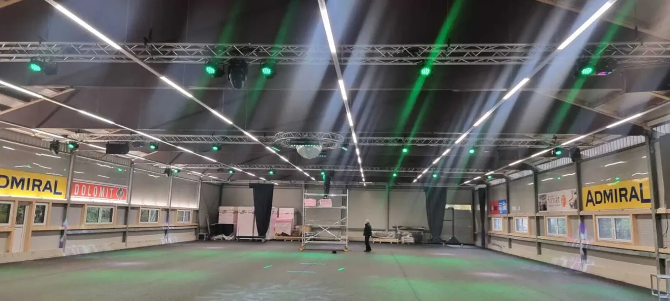 Ein Innenbereich ist mit grünen Lichtern ausgestattet. Eine Person steht neben einem weißen Gerüst mit rosa Kisten.