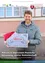 Ein Mann in einer Jacke hält eine Adventsbox und trägt einen Weihnachtsmannhut. Er lächelt und steht vor einem Gebäude mit Weihnachtsthema.