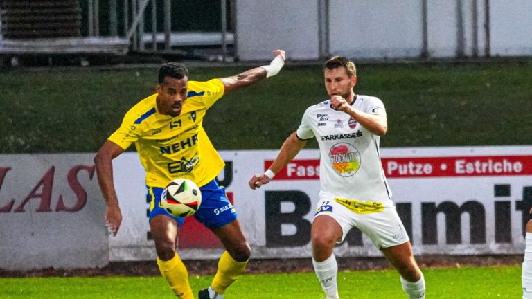 Zwei Fußballspieler konkurrieren auf einem Feld. Einer trägt ein gelbes Trikot, der andere ein weißes. Sie versuchen beide, den Ball zu kontrollieren.