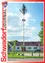 Ein geschmückter Maibaum steht in einem Park neben einem Haus mit rotem Dach, unter einem teilweise bewölkten Himmel. Es gibt Bäume, eine Bank und ein geparktes Auto in der Umgebung.