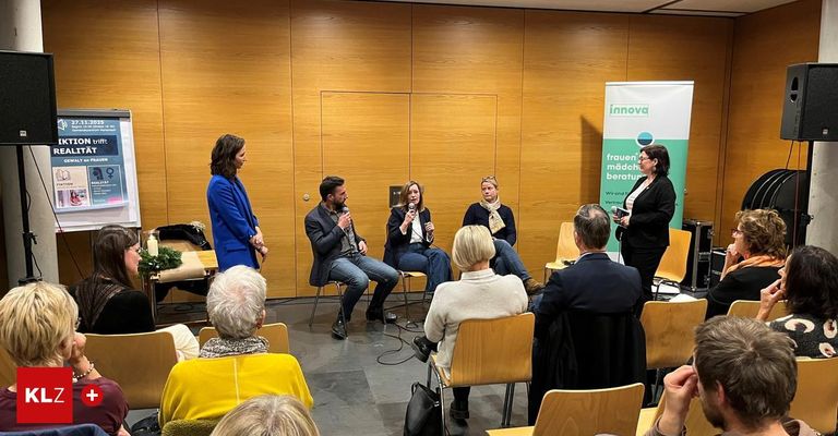 Eine Podiumsdiskussion mit fünf Personen, zwei Frauen und drei Männern, in einem Raum mit Holzwänden und Holzstühlen. Eine Frau steht auf der rechten Seite des Raumes.