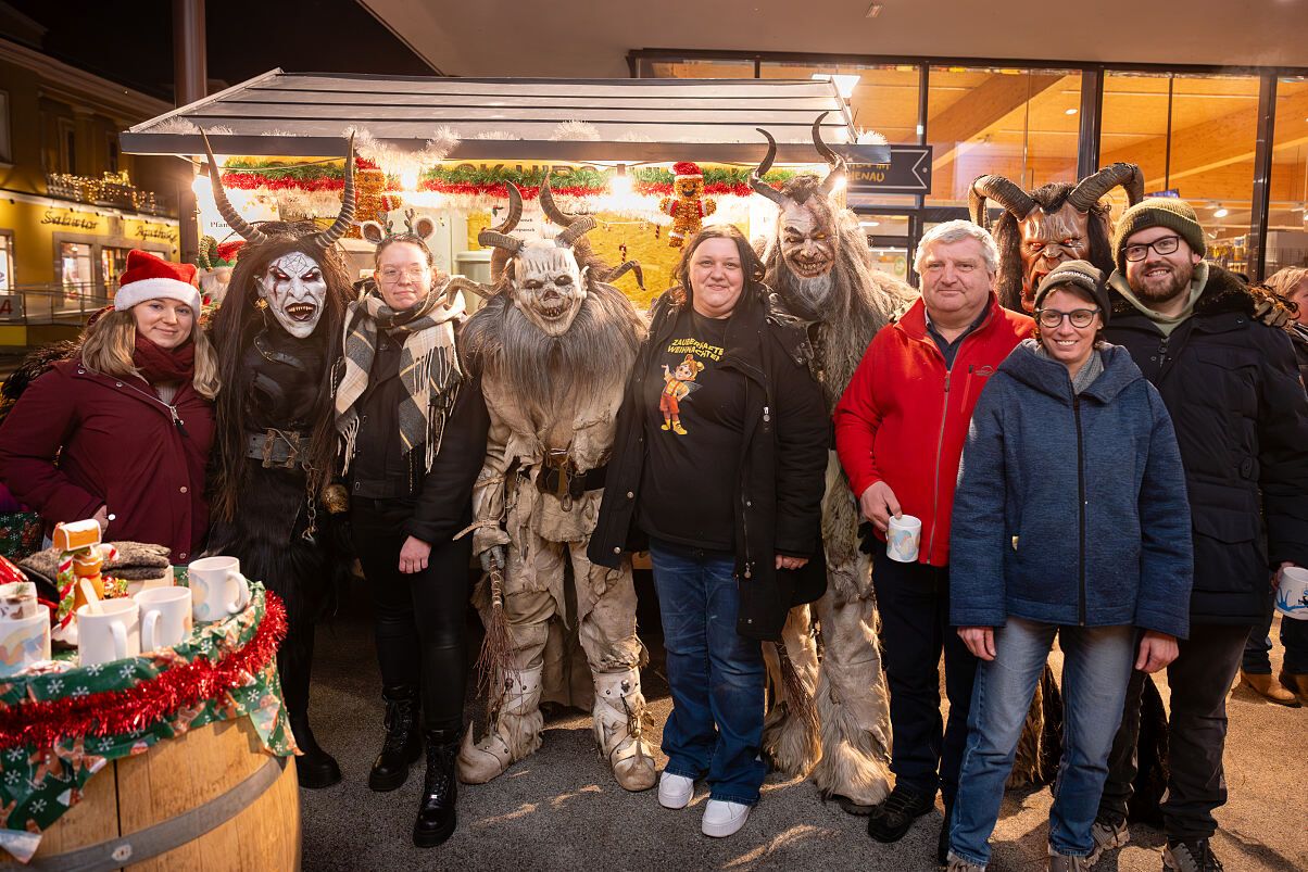 Eine Gruppe von Menschen, die in gruseligen Kostümen gekleidet sind, posiert für ein Foto. Einige von ihnen halten Tassen. Links befindet sich ein Fass und dahinter eine Glaswand.