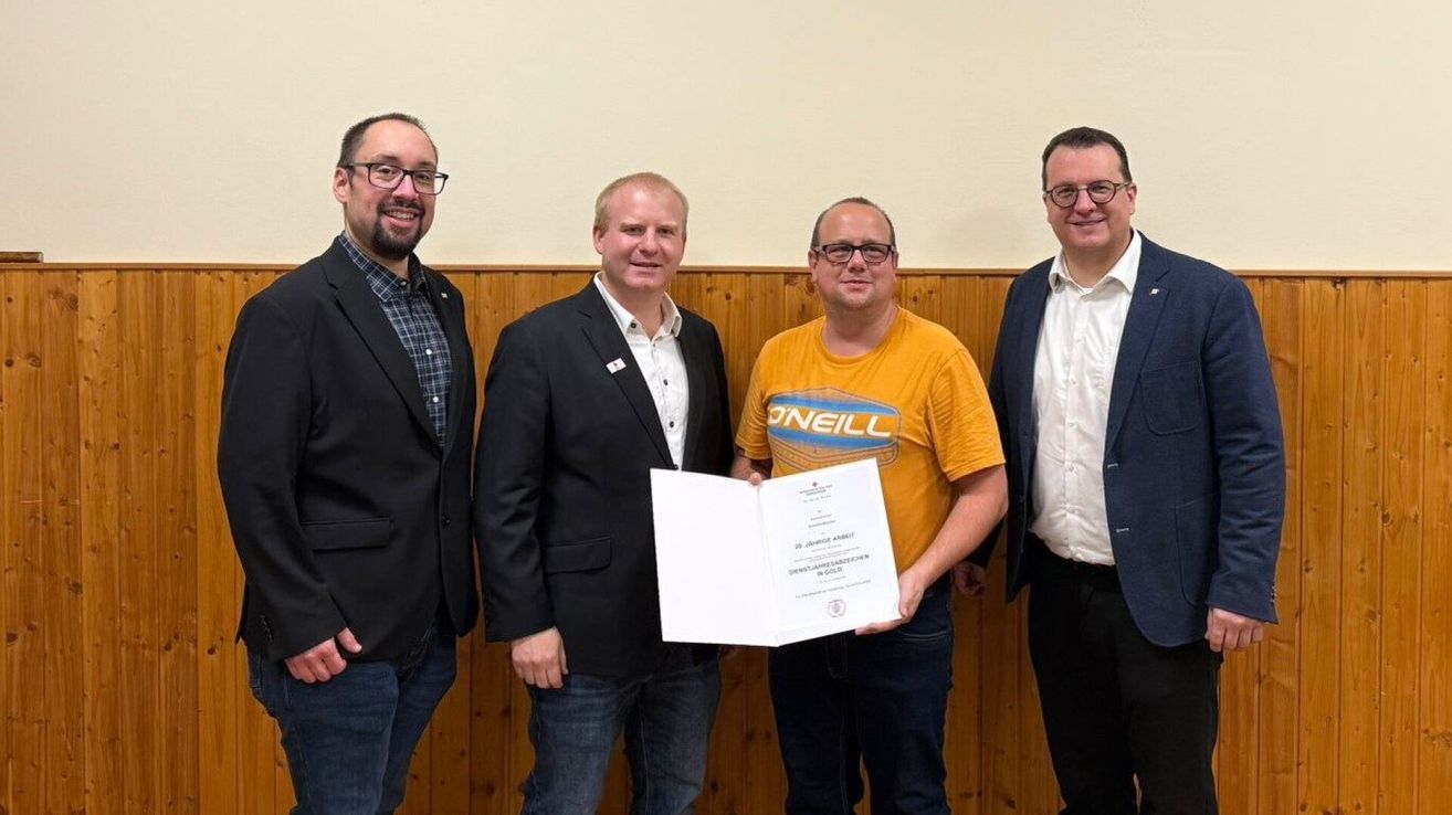 Four men stand together holding a certificate, one in a yellow shirt with Neill written on it.