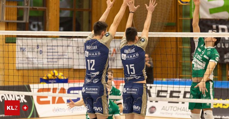Two men in blue jerseys celebrate after a successful volleyball play. One player has the number 12, and the other has 15 on their jerseys.