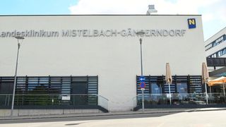 The exterior of a medical facility named 'Klinikum Mistelbach-Ganserndorf' with a glass entrance and a lamp post in front.
