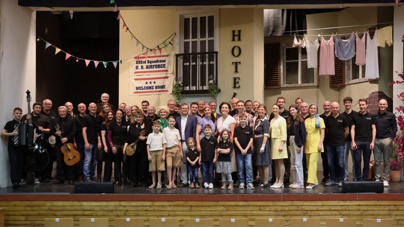 Eine Gruppe von Menschen steht auf einer Bühne mit einem Banner, das 293rd Squadron U.S. Air Force und Willkommen zu Hause sagt. Dahinter befindet sich ein Gebäude mit dem Wort Hotel an der Wand.