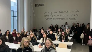 A classroom with students seated at tables, an inspirational quote on the wall, and a projector hanging from the ceiling.