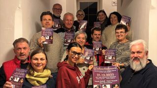 A group of people posing for a photo, holding up flyers for a Christmas concert. The flyer has the date 21.12.2025, and the names Fausta Galleli, Pablo Grande, and Nina Bernsteiner. The event is taking place at the Pfarrkirche Pinkafeld.