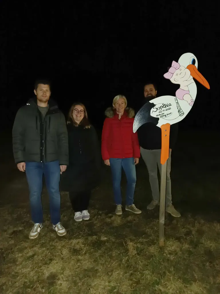 Vier Personen posieren bei Nacht für ein Foto mit einem Storch-Ausschnitt. Der Storch hat eine Nachricht für Sophia.