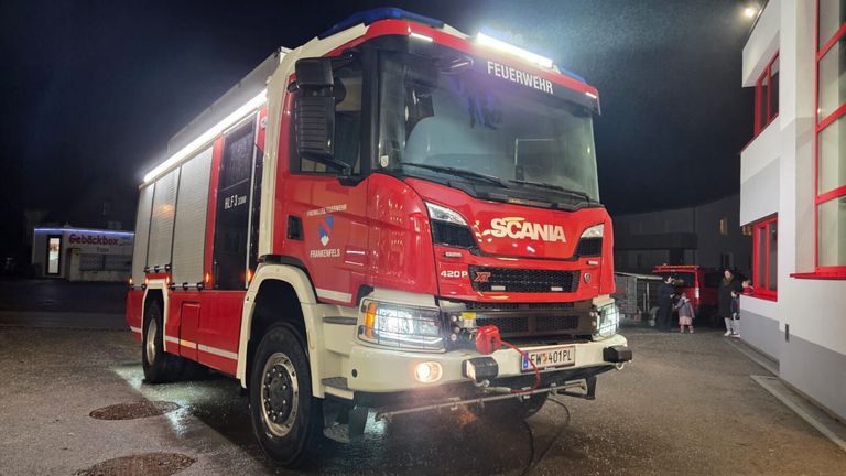 Ein roter Scania-Feuerwehrwagen steht bei Nacht geparkt, Scheinwerfer eingeschaltet, und das Kennzeichen lautet EW 401 PL. Das Wort Scania ist auf der Front aufgedruckt.