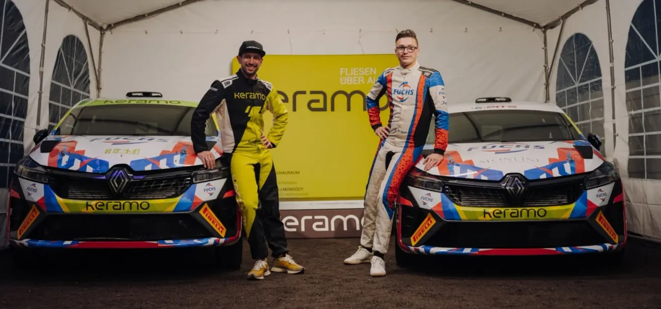 Zwei Rennfahrer stehen neben ihren bunten Autos vor einem gelben Banner. Beide tragen Helme und Rennanzüge mit verschiedenen Logos.