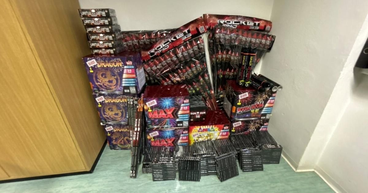 A room with multiple boxes of fireworks stacked on a green floor. Each box has different themes and names, such as Dragon, Rocket, and Boom Boom. The fireworks are in various colors and shapes.