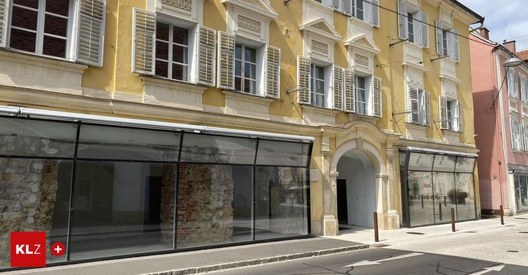 Ein gelbes Gebäude mit weißen Fensterläden hat eine Ziegelmauer in der Mitte des Glaseingangs. Es hat einen steinernen Bogeneingang.