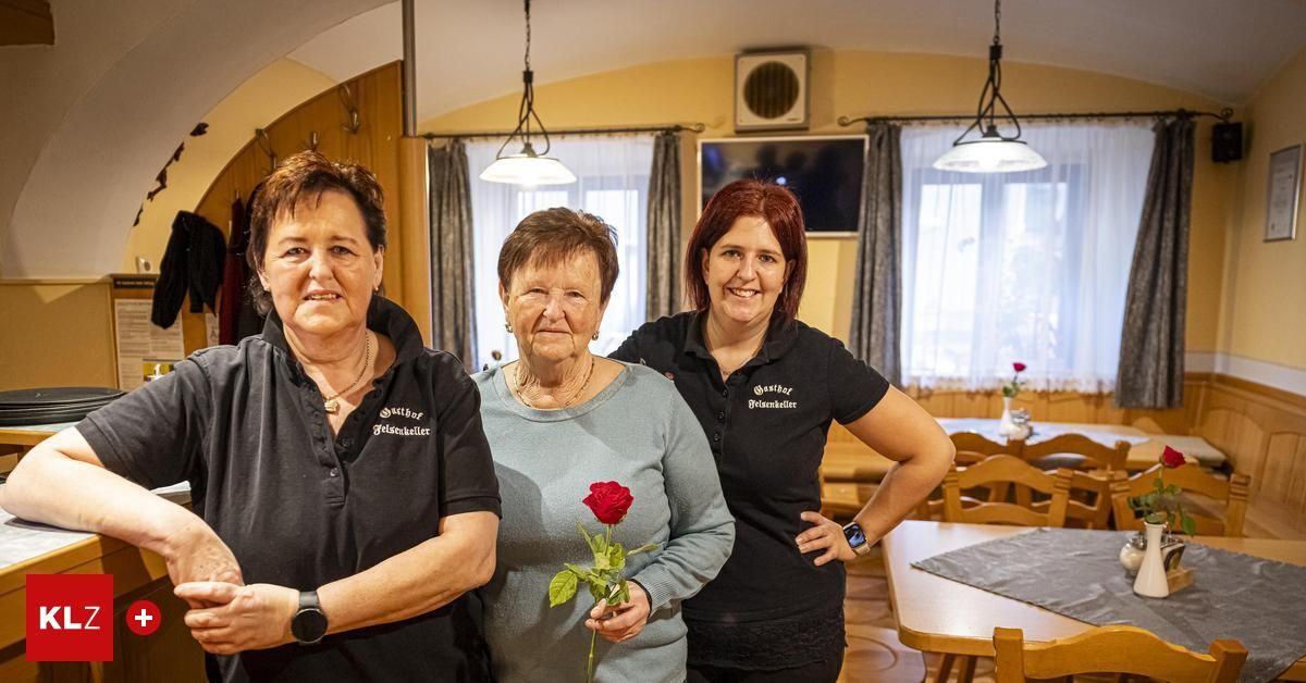 Drei Frauen stehen zusammen in einem Raum. Die Frau links und rechts trägt schwarze Hemden, während die Frau in der Mitte ein blaues Hemd trägt und eine rote Rose hält.