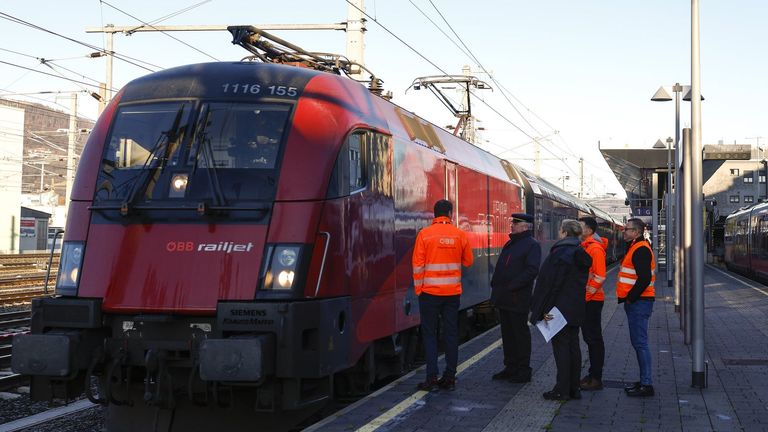 Ein roter Zug mit der Nummer 1116 155 steht am Bahnsteig, und mehrere Personen in orange Westen stehen in der Nähe. Der Zug hat das Wort railjet an der Seite.