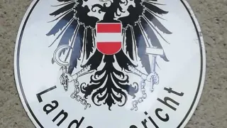 A round white sign displays a black eagle with a crown, holding a sword and keys. The Austrian flag is in the eagle's chest. The text reads 'Landesgericht'.