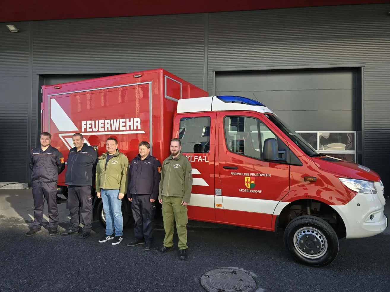 Five men are standing in front of a red fire truck with the word Feuerwehr on the side.