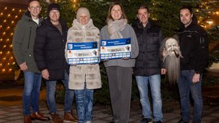 Several people stand in front of a Christmas tree holding checks for 604 euros. They are smiling for the camera.