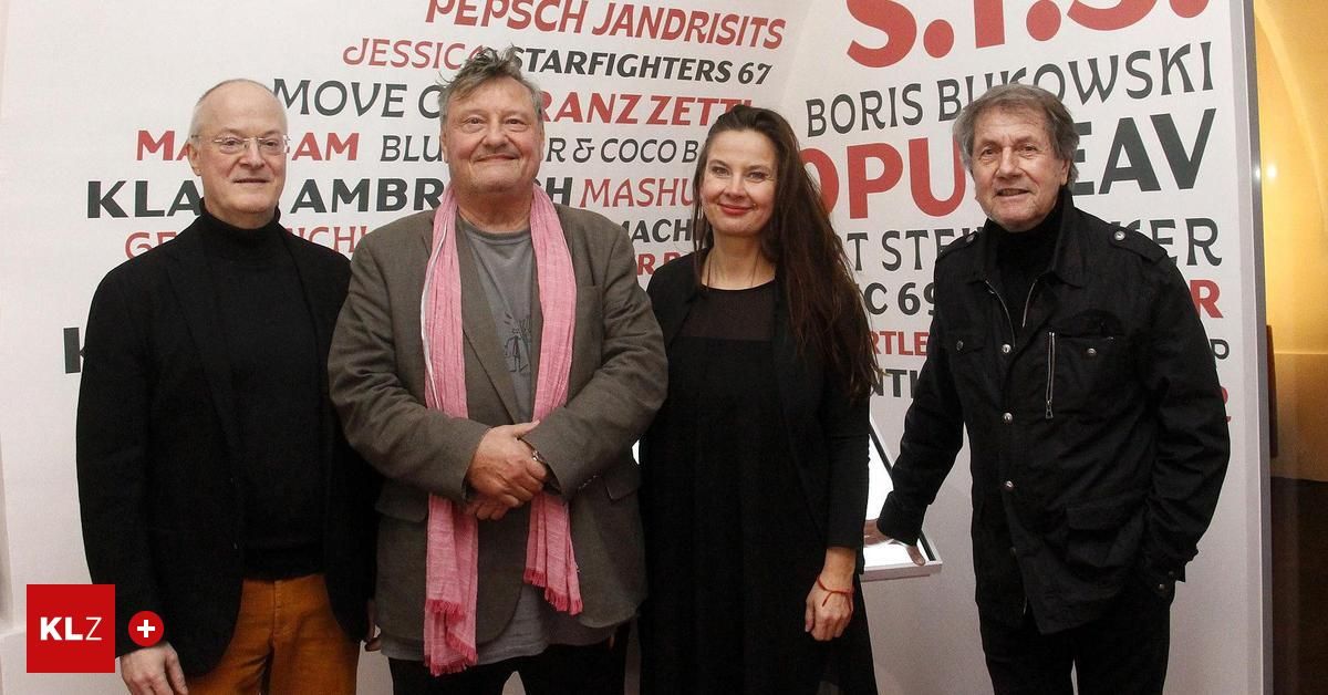 Four individuals pose for a photo in front of a vibrant, colorful backdrop featuring various texts and logos.