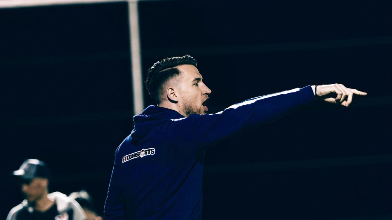 Ein Mann in einem blauen Hoodie mit weißem Text auf dem Rücken gibt bei Nacht auf einem Feld Anweisungen.