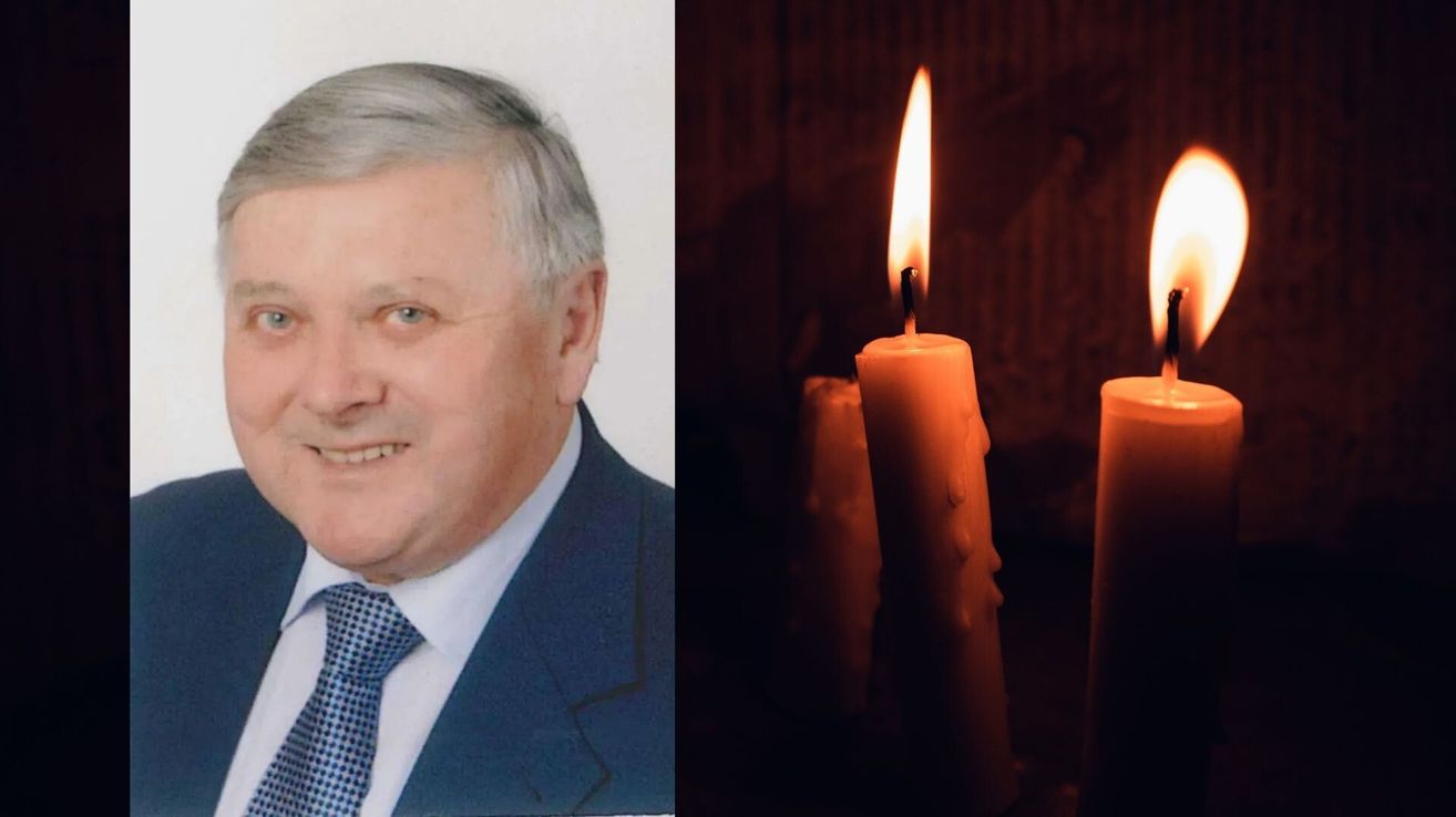 Ein Foto eines lächelnden Mannes in Anzug und Krawatte mit brennenden Kerzen im Hintergrund.