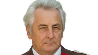 A man with gray hair, wearing a military uniform, has a serious expression on his face. He is looking straight ahead.