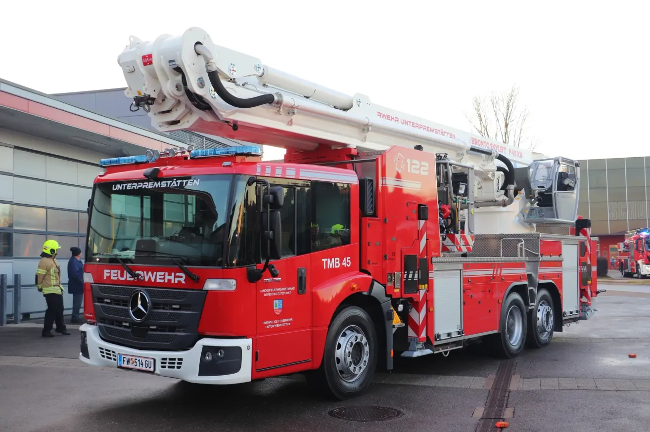 Ein roter Feuerwehrwagen mit der Nummer 45 steht vor einem Gebäude. Oben hat er eine weisse Leiter.