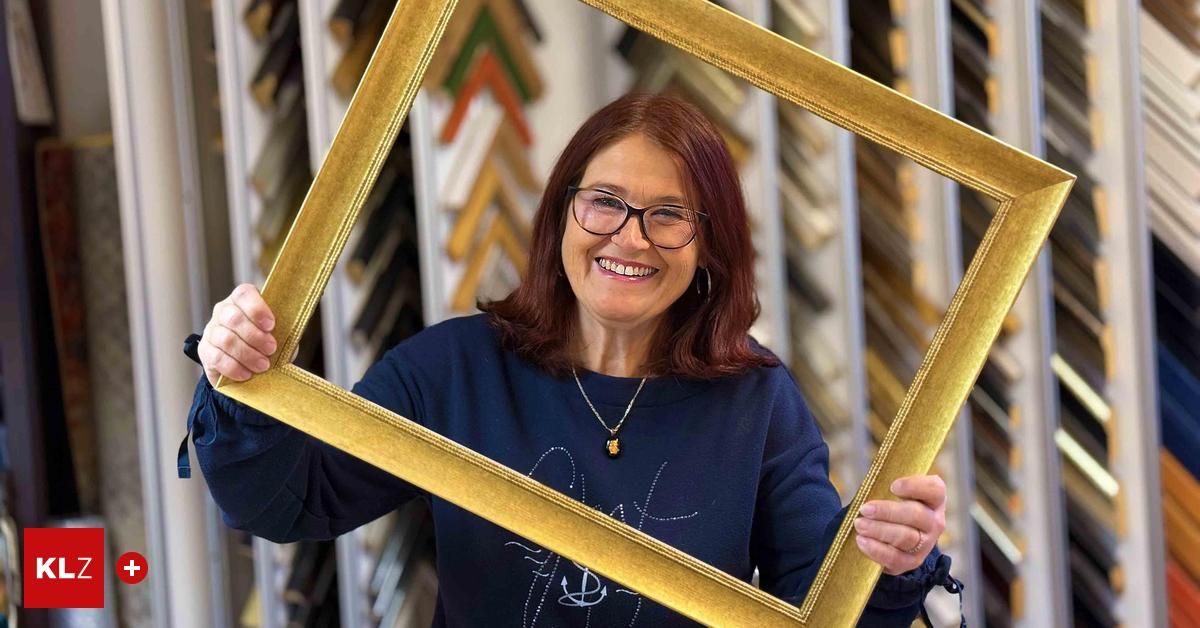 Eine Frau mit Brille und blauem Shirt hält einen goldenen Bilderrahmen vor sich und lächelt.