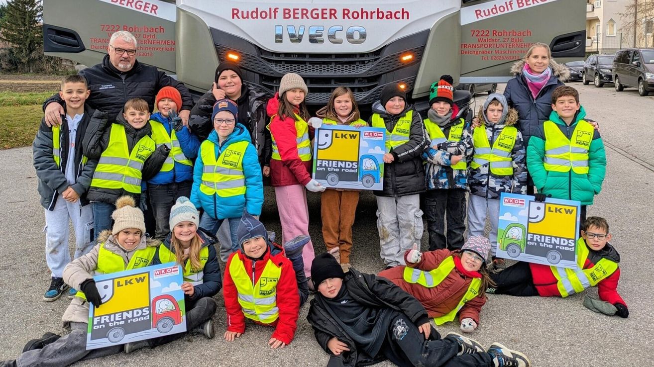 Kinder und Erwachsene in Warnwesten posieren mit einem Schild, das 'Freunde auf der Straße' vor einem IVECO-LKW steht.