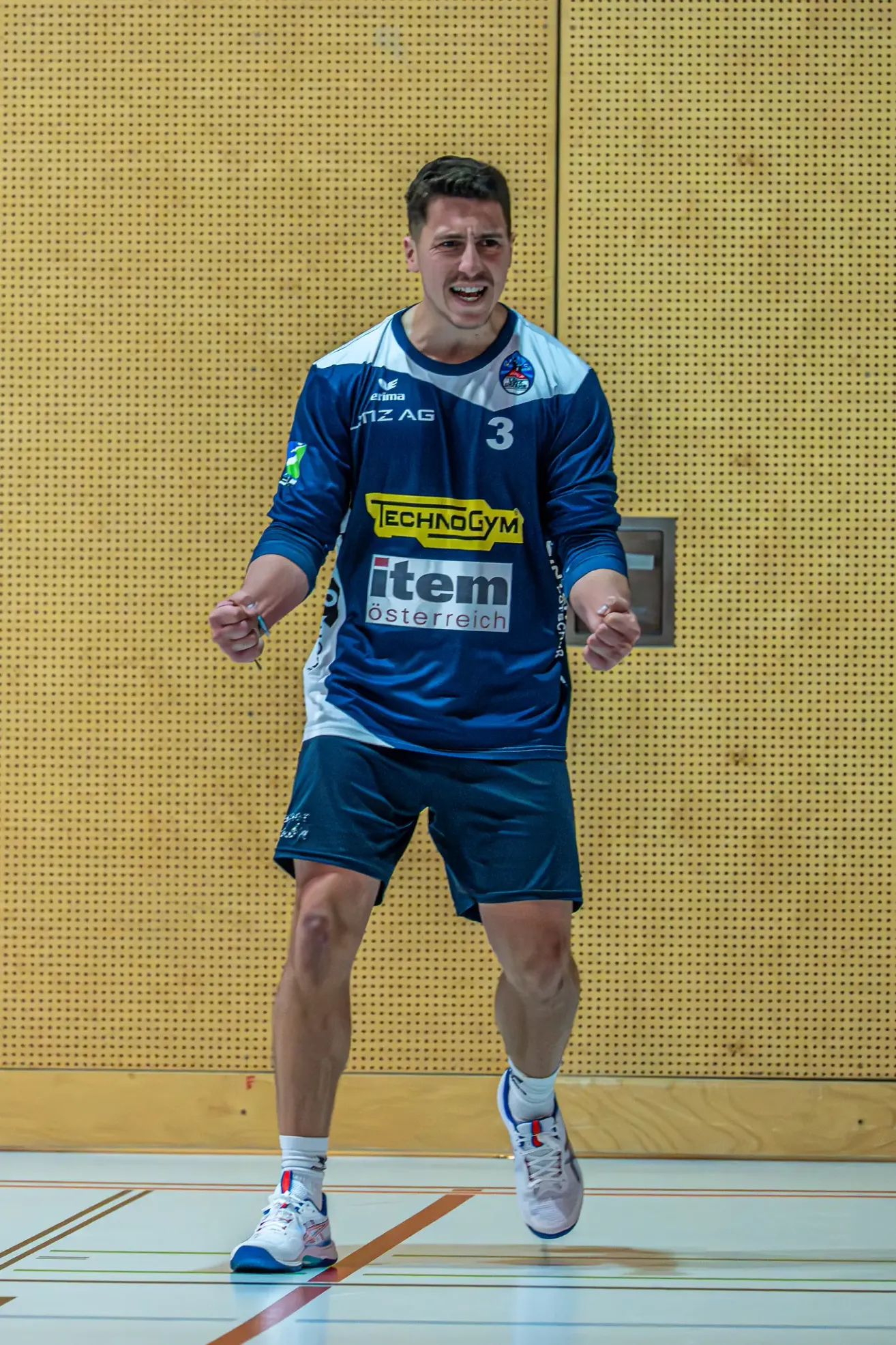 Ein lächelnder Mann in einem blau-weißen Sporttrikot mit der Nummer 3 und item osterreich darauf geht nach vorne.