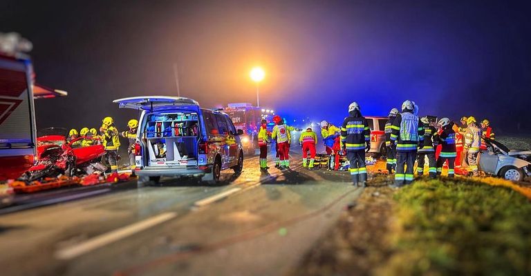 Rettungskräfte kümmern sich an der Unfallstelle bei Nacht um verletzte Personen auf einer Straße.