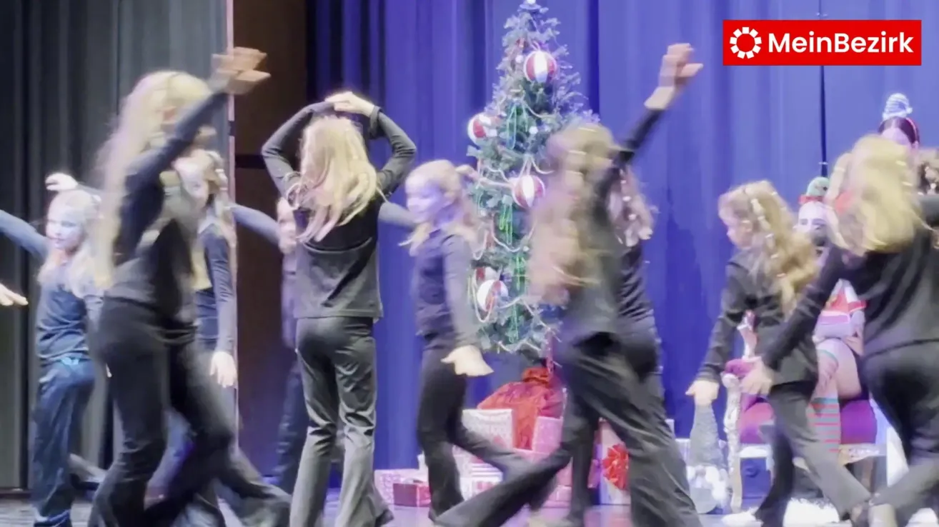 Eine Gruppe von Frauen auf der Bühne, möglicherweise im Tanz, vor einem geschmückten Weihnachtsbaum mit roten und weißen Kugeln.