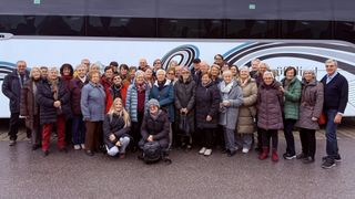 A group of people in winter clothing pose for a photo in front of a bus.