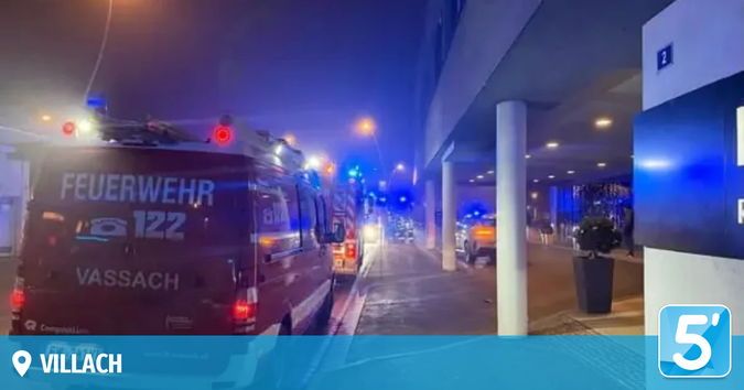 Einsatzfahrzeuge, darunter ein Feuerwehrwagen, sind am Straßenrand geparkt, wobei die Blaulichter blinken. Ein Gebäude mit einem Schild mit der Aufschrift '2' ist zu sehen. Ein Topf steht im Vordergrund.