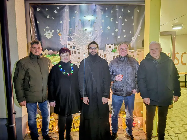 Fünf Personen stehen vor einer dekorativen Kulisse mit einer Stadt und Sternen. Eine Person trägt eine Halskette mit bunten Lichtern.