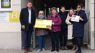 Fünf Personen stehen auf einem Holzboden und halten einen Scheck über 500 Euro. Sie scheinen für ein Foto zu posieren. Der Scheck hat Text und Zahlen. Die Person auf der linken Seite trägt einen Gürtel.