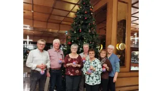 Eine Gruppe von Menschen steht vor einem Weihnachtsbaum in einer Lobby, jeder hält eine lila Kugel.